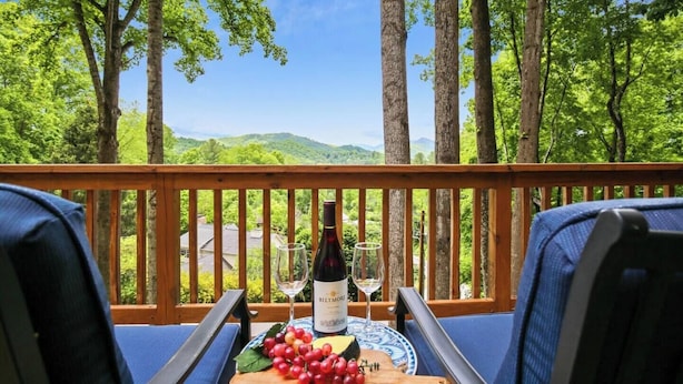 Eine Holzterrasse mit zwei blauen Stühlen, einem Tisch mit einer Weinflasche, Gläsern und einer Platte mit Trauben.