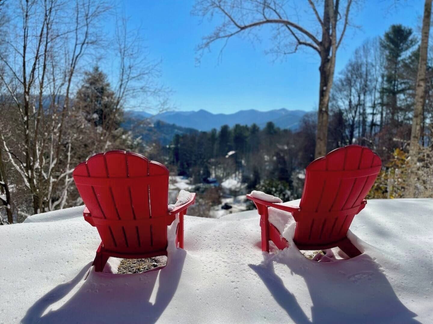 Kaksi punaista Adirondack-tuolia, joiden edessä avautuu lumipeitteinen maisema ja kauempana näkyy vuoria.