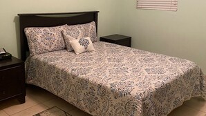 A bedroom with a bed, nightstands, a bedside table, a wall-mounted picture, a window with blinds, and a red and beige rug. - Close to Beach and Fish Fry (Nassau)