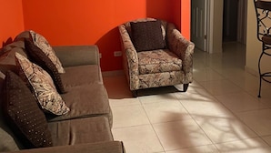 A living room with a brown sofa and patterned armchair, orange walls, and a tiled floor. - Close to Beach and Fish Fry (Nassau)