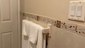 A bathroom with a white towel hanging on a towel rack, a door, and a wall with a light switch and decorative tiles. - Close to Beach and Fish Fry (Nassau)