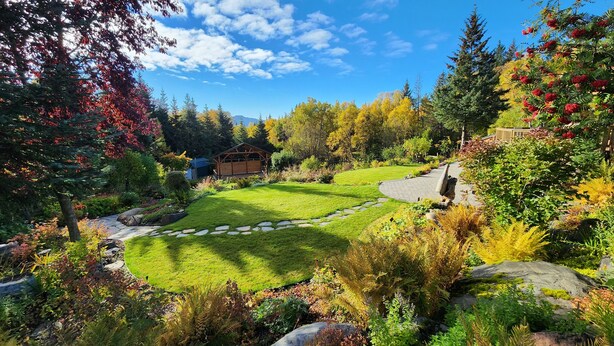 Un jardin bien entretenu, agrémenté d’une structure en bois, de chemins en pierre et d’une grande variété de plantes et d’arbres.