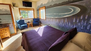 Une chambre à coucher avec un grand lit, deux chaises, une petite table et un téléviseur.