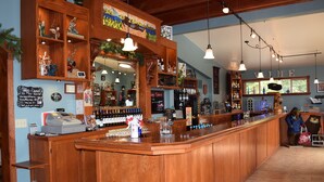 Un espace bar avec des comptoirs en bois, des étagères remplies de bouteilles et une caisse enregistreuse.
