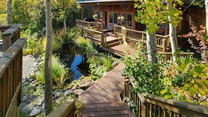 Une terrasse en bois menant à un chalet offrant une vue sur un étang et les arbres environnants.