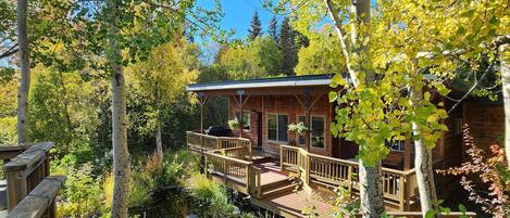 A wooden deck leading to a cabin with a view of a pond and surrounding trees.