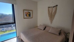 Une chambre avec un grand lit, une décoration murale en macramé et un tableau encadré.