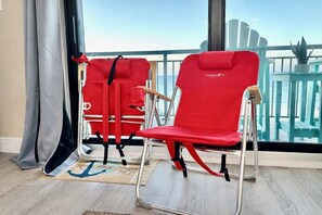 Two red chairs with a view of the ocean through a balcony railing.