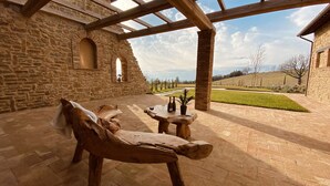 A stone building with a wooden bench and table, a potted plant, and a view of a green landscape. - Villa Antica Dimora intera struttura - Homelike Villas (San Donato)