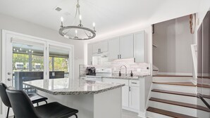 Una cucina moderna con isola centrale, mobili bianchi e una scala che conduce a un piano superiore.
