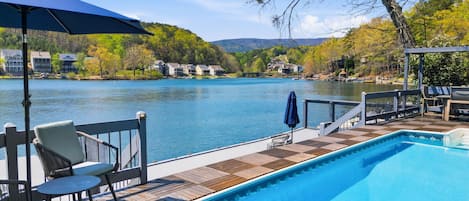 Uma piscina com um deck, cadeiras e um guarda-sol.