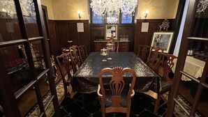 Uma sala de jantar formal com uma grande mesa redonda, cadeiras elaboradas, um candelabro e um tapete estampado.