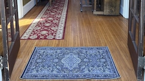 Um hall espaçoso com um lustre imponente, uma escada de madeira e um tapete com padrão em vermelho e azul que conduz aos degraus.