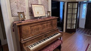 Um piano de cauda em uma sala ampla, com um candelabro, certificados emoldurados e um tapete estampado.
