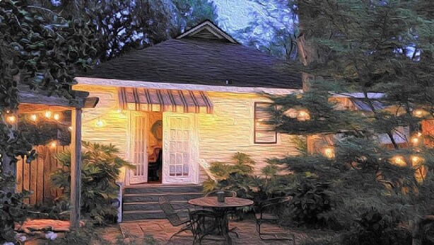 A cozy cottage with a wooden exterior, a porch with chairs, and string lights.