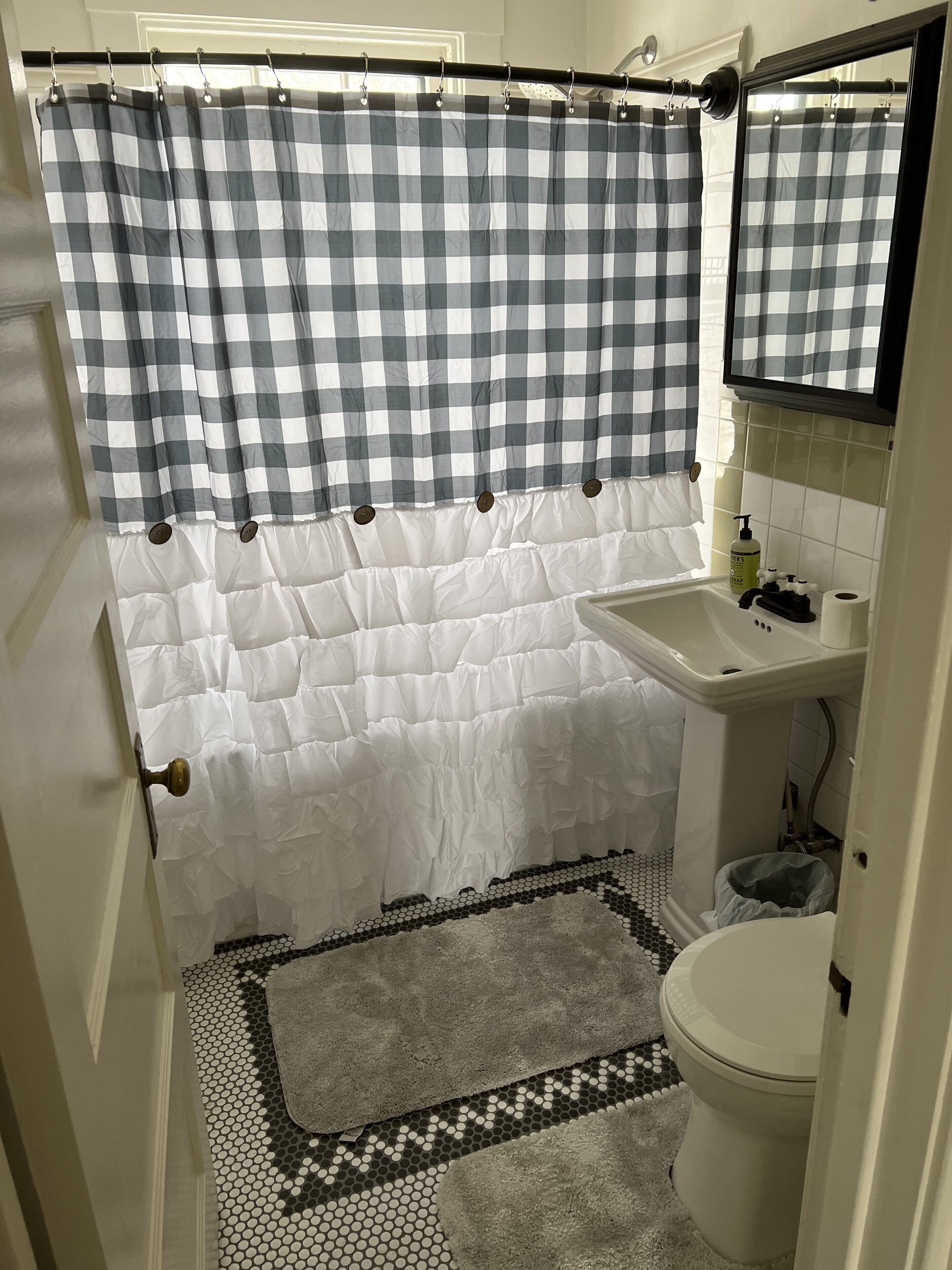 A bathroom with a checkered shower curtain, a white sink, a mirror, and a patterned rug.