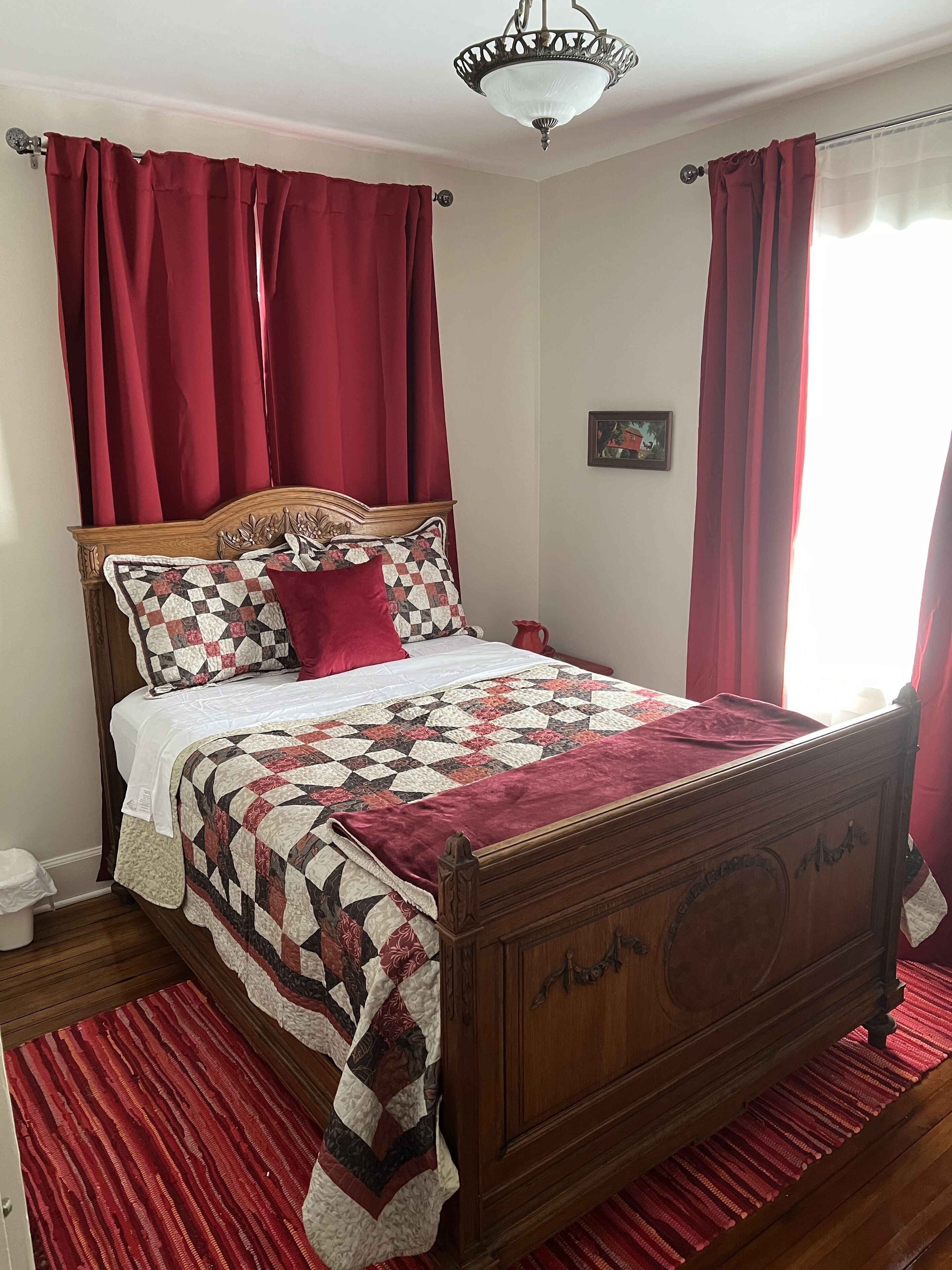 A neatly made bed with a wooden headboard, red curtains, and a patterned quilt.