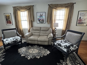 Un salon avec un canapé beige, deux fauteuils à motifs, un tapis à motifs et une lampe.