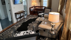 A living room with a sofa, a TV, a lamp, a patterned rug, and a dining area. - Charming Carriage House near VanderVeer Park (Davenport)