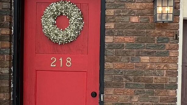 A red door with the number 218, a wreath above it, and a brick wall with a lantern to the right. - Charming Carriage House near VanderVeer Park (Davenport)