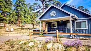 Une cabane avec une véranda, une enseigne indiquant « Cedarwood », et une clôture en bois à l’avant.