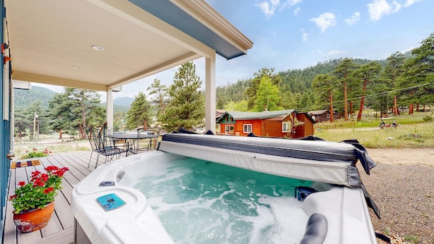 Un bain à remous avec une terrasse en bois et une vue sur un chalet situé dans une zone boisée.