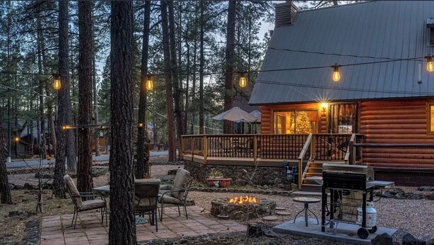 A log cabin with a deck, outdoor seating, a fire pit, and string lights.