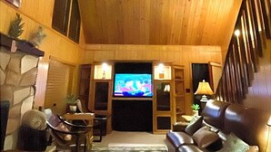 A wooden interior with a fireplace, a television, leather seating, and a staircase.