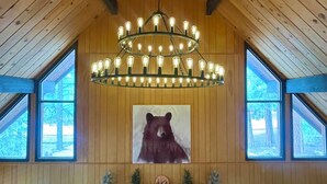 A room with a stone fireplace, a bear painting, and a chandelier.