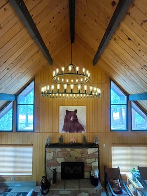 A room with a stone fireplace, a bear painting, and a chandelier.