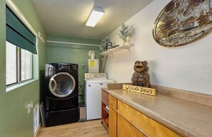 Een kleine keuken met een wasmachine, een kookplaat en een houten aanrecht met een bordje.