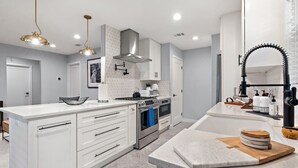 Una cucina moderna con mobili bianchi, elettrodomestici in acciaio inossidabile e luci a sospensione.