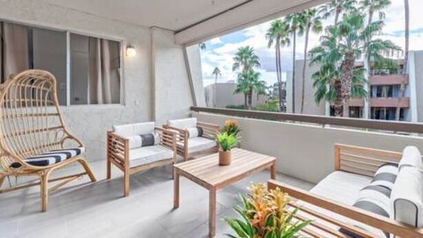 Een balkon met rieten stoelen, een houten tafel en een bank.