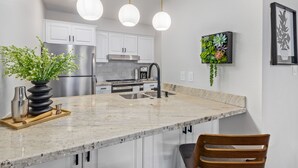 Een moderne keuken met witte kasten, een marmeren aanrechtblad, roestvrijstalen apparatuur en hanglampen.