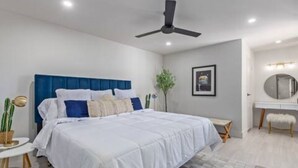 Een moderne slaapkamer met een groot bed, een plafondventilator, een nachtkastje en een klein bureau met stoel.