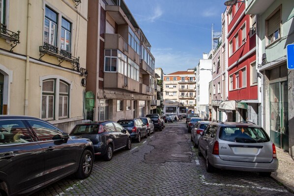Una estrecha calle adoquinada bordeada de coches aparcados y edificios de varios pisos.