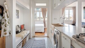 A compact kitchen with a washing machine, a sink, and a window with curtains. - JOIVY Cosy 2-bed flat w/desk in Arroios (Lisbon)