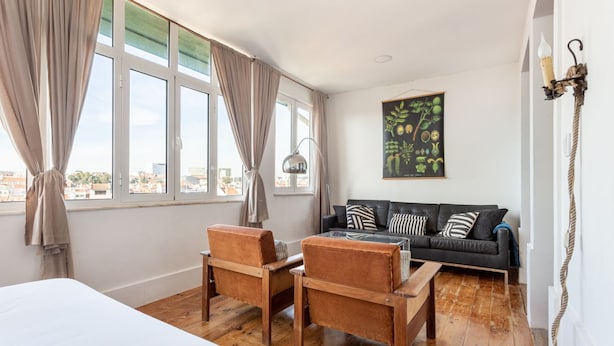 A room with a bed, two chairs, a small table, a sofa, a lamp, and a painting on the wall. - JOIVY Cosy 2-bed flat w/desk in Arroios (Lisbon)
