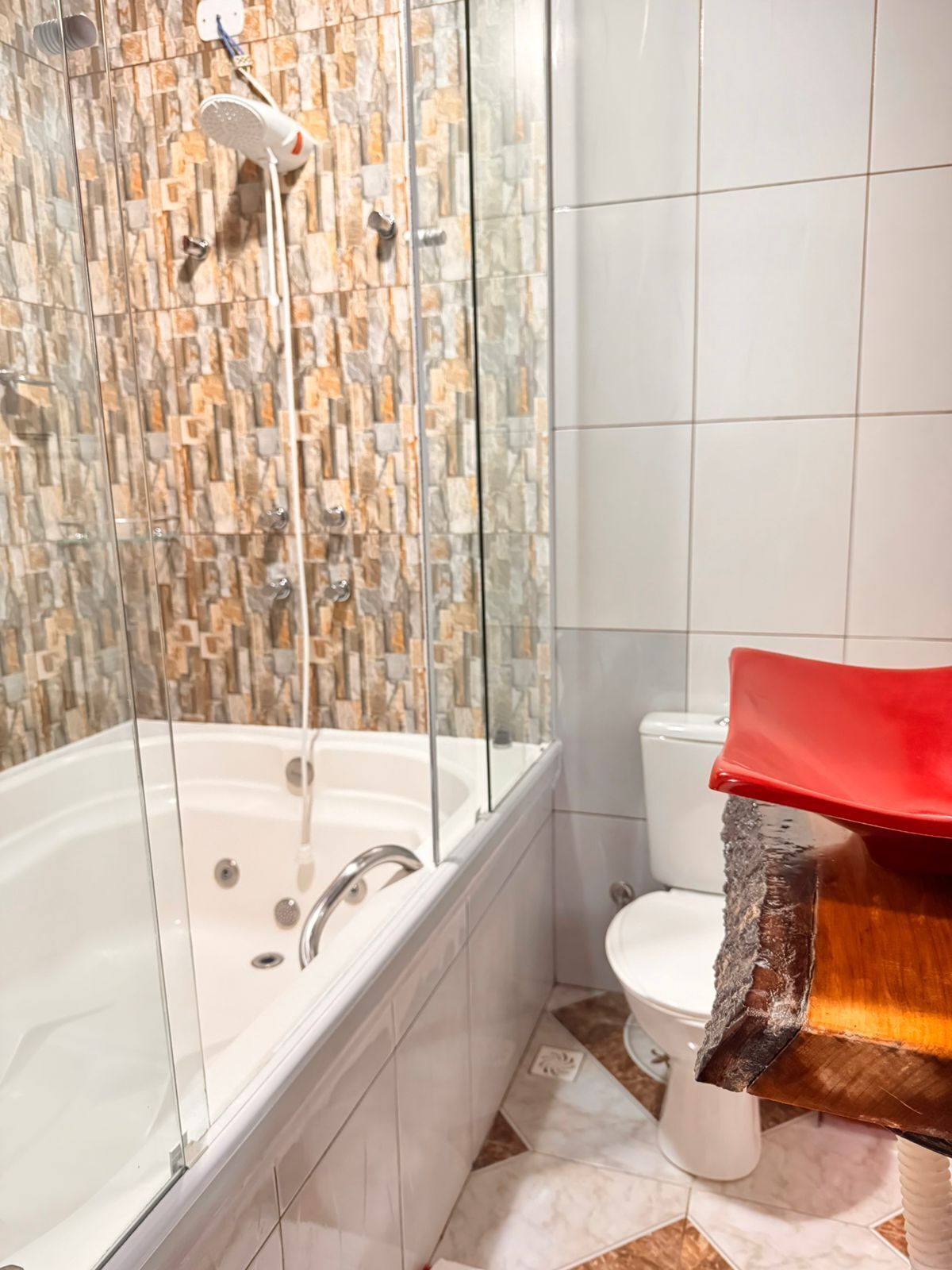 A bathroom with a glass-enclosed shower, a white toilet, and a wooden vanity with a red countertop.
