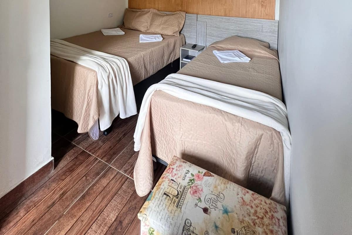 Ein Zimmer mit zwei Betten, Holzboden und einem kleinen Tisch mit einer blumigen Tischdecke.