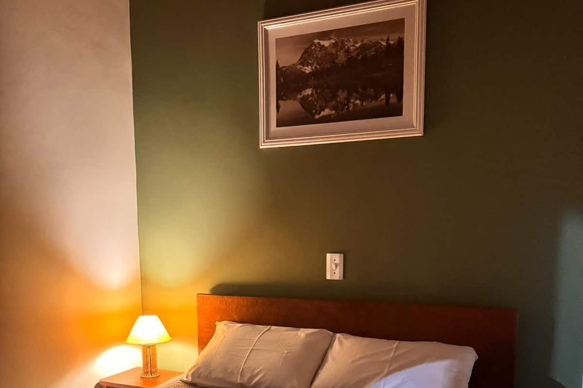 Ein ordentlich bezogenes Bett mit Holz-Kopfteil, einer Nachttischlampe und einem gerahmten Bild an der Wand.