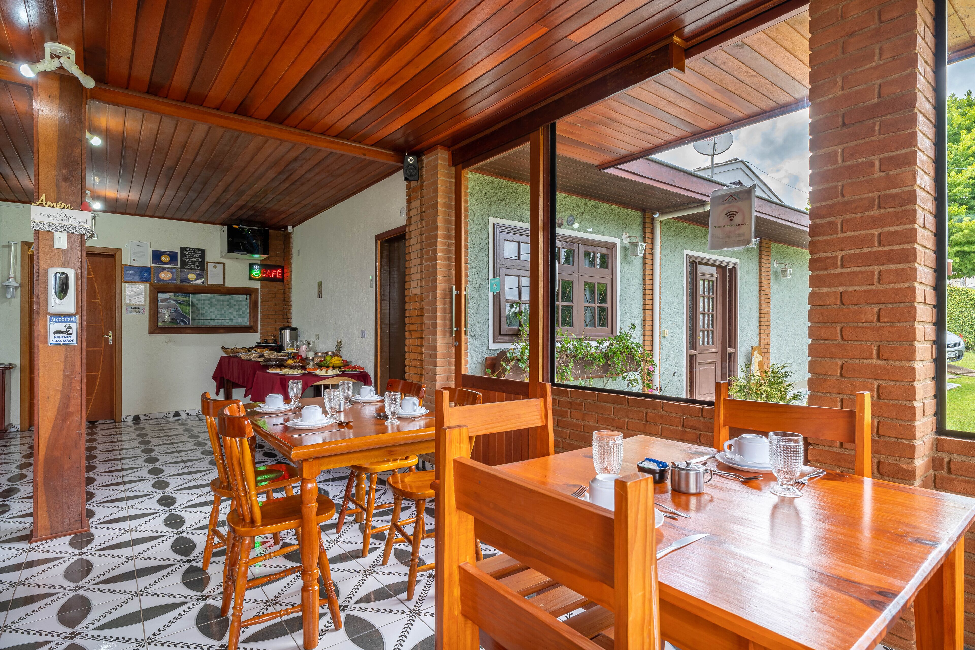 A dining area with wooden tables and chairs, a tiled floor, and a brick wall.