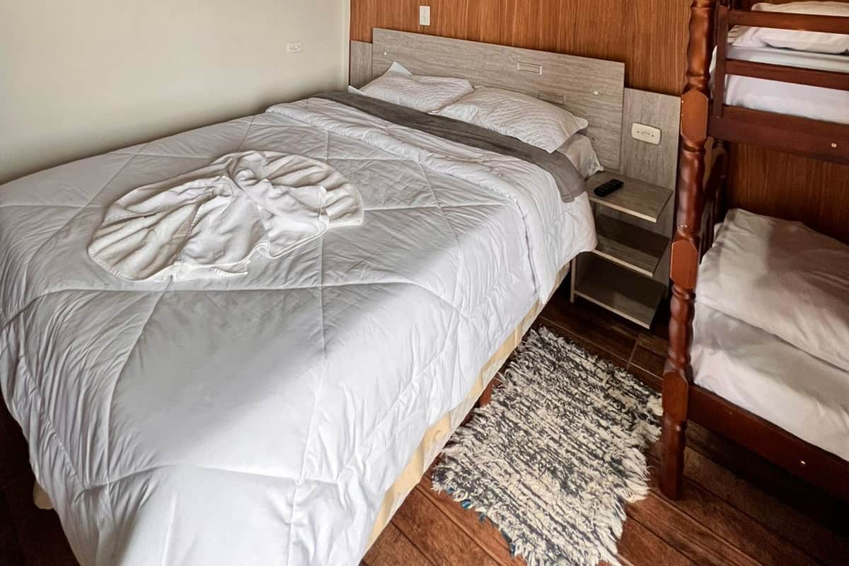 Ein Schlafzimmer mit Holzboden, einem Etagenbett, einem Einzelbett mit Steppdecke, einem Nachttisch und einem Teppich.
