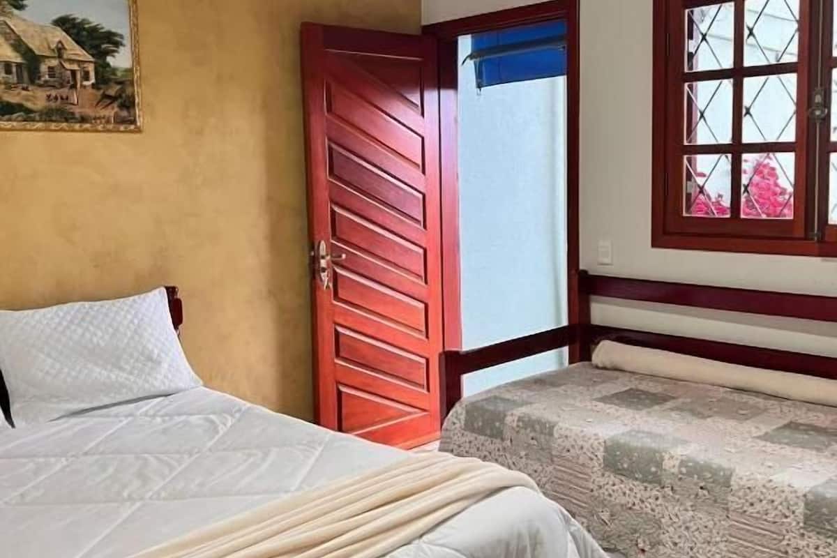 Ein Zimmer mit einem Bett, einer Holztür, einem Fenster mit Blick und einem Gemälde an der Wand.