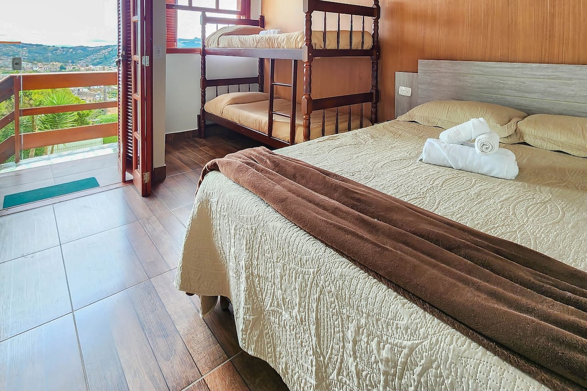 Ein Schlafzimmer mit Holzbalkendecke, einem Stockbett, einem großen Bett mit Decke und Blick durch eine offene Tür.