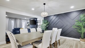 A modern dining area with a wooden table and white upholstered chairs, a black accent wall, and a hanging light fixture.
