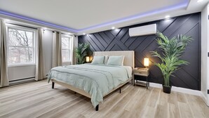 A modern bedroom with a bed, bedside tables, a potted plant, and a wall-mounted air conditioner.