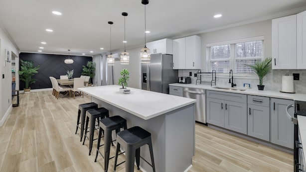 A modern kitchen with a large island, bar stools, stainless steel appliances, and pendant lighting.