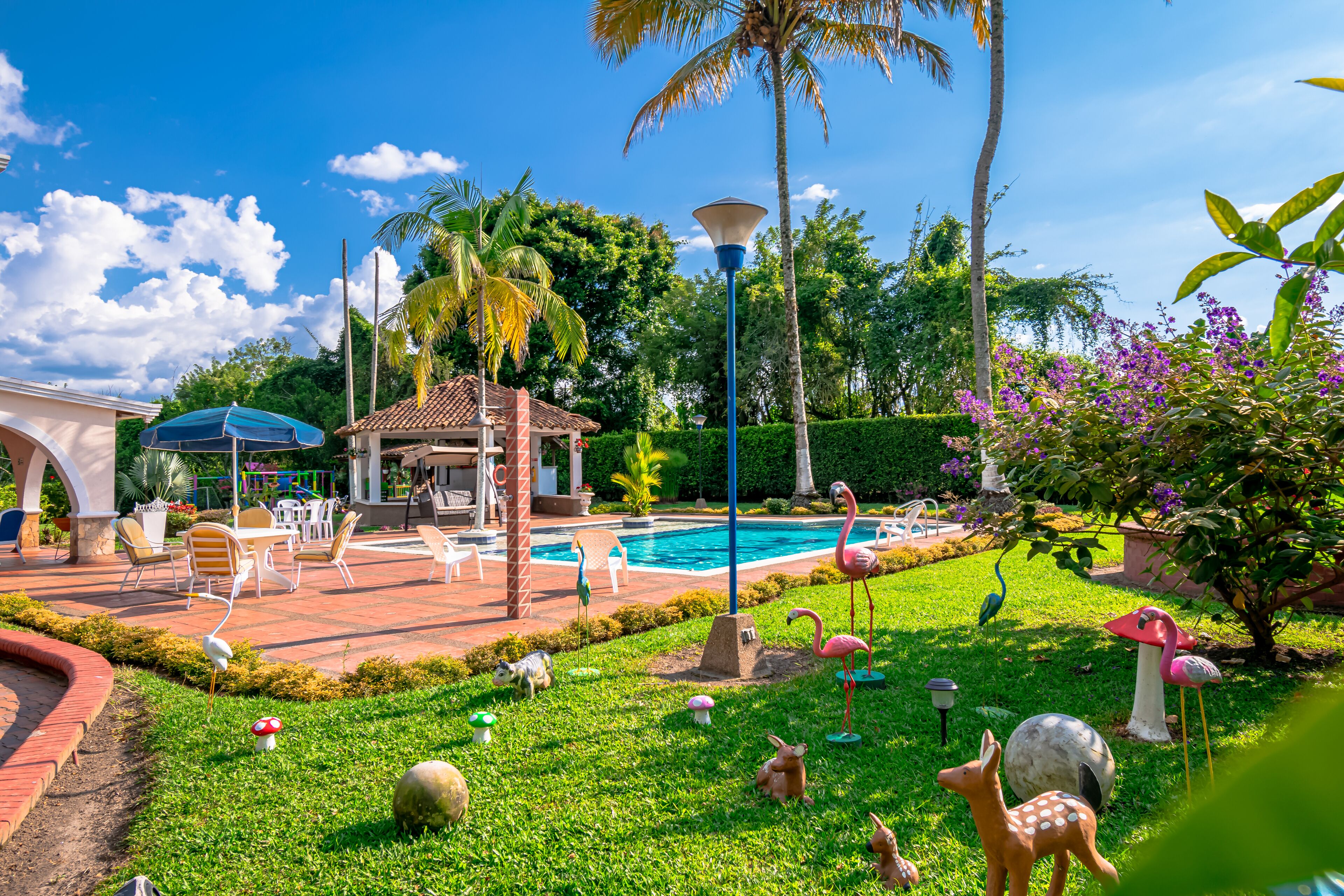 A pool area with a gazebo, palm trees, and various garden statues.