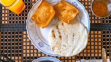 A breakfast plate with toast, flatbread, scrambled eggs, butter, and a glass of orange juice.